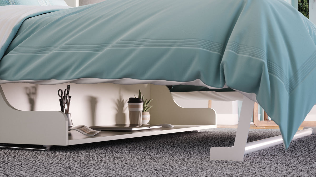 A close-up under the bed of a Murphy Bed with a desk. The desk is level and decorated with office supplies and a closed laptop. The bed is dressed with a light blue-green duvet cover, shown in a modern bedroom setting.