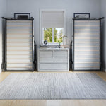 Room with gray walls, a window with blinds, and two black metal twin beds lifted up against the wall.