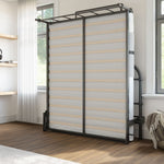 foldable black metal bed lifted up against the wall with two windows, wood flooring and a grey carpet