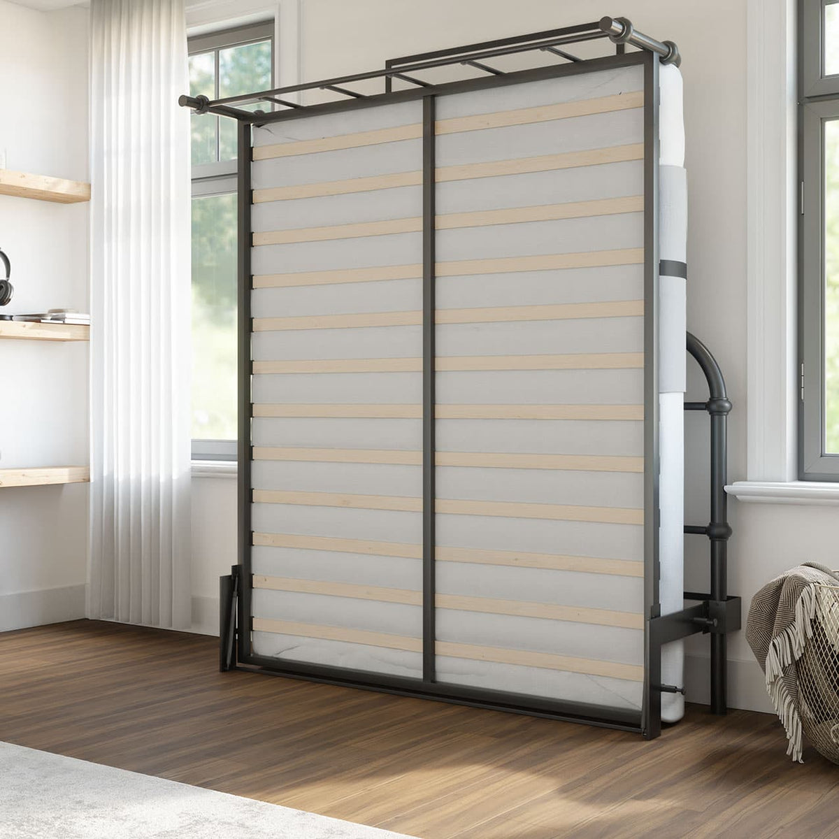 foldable black metal bed lifted up against the wall with two windows, wood flooring and a grey carpet
